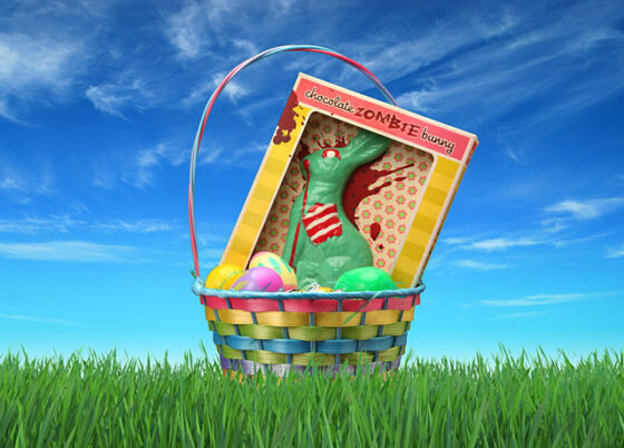 A chocolate zombie bunny in a box sitting in a colorful Easter Basket on green grass with a bright blue sky behind.